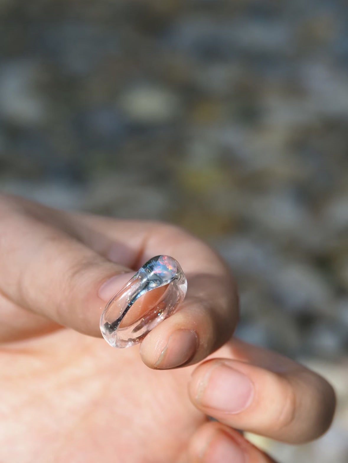 Clear glass ring with lab-grown opal held between fingertips to show its scale.