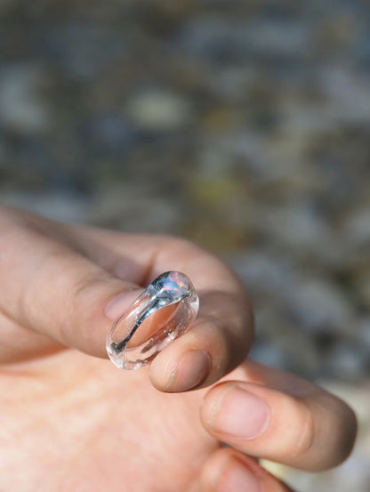 Clear glass ring with lab-grown opal held between fingertips to show its scale.